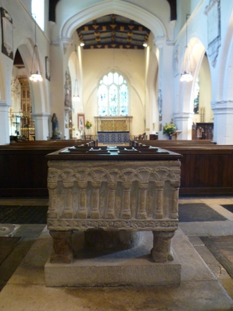 The Norman font, with the old nave and chancel in the background